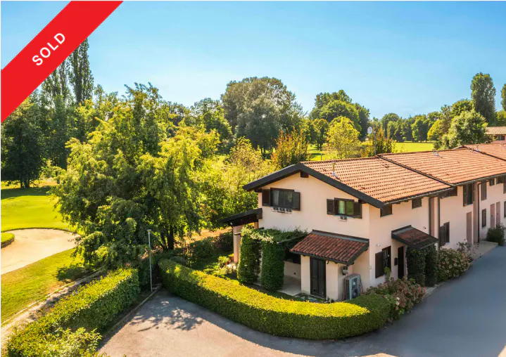 A sold townhouse with a red tile roof, surrounded by green trees and a golf course.