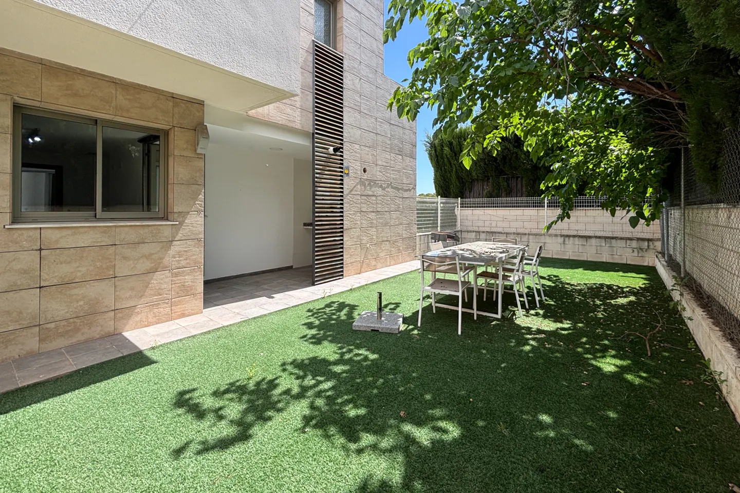 Backyard view of a two-story house with a table and chairs on green grass.
