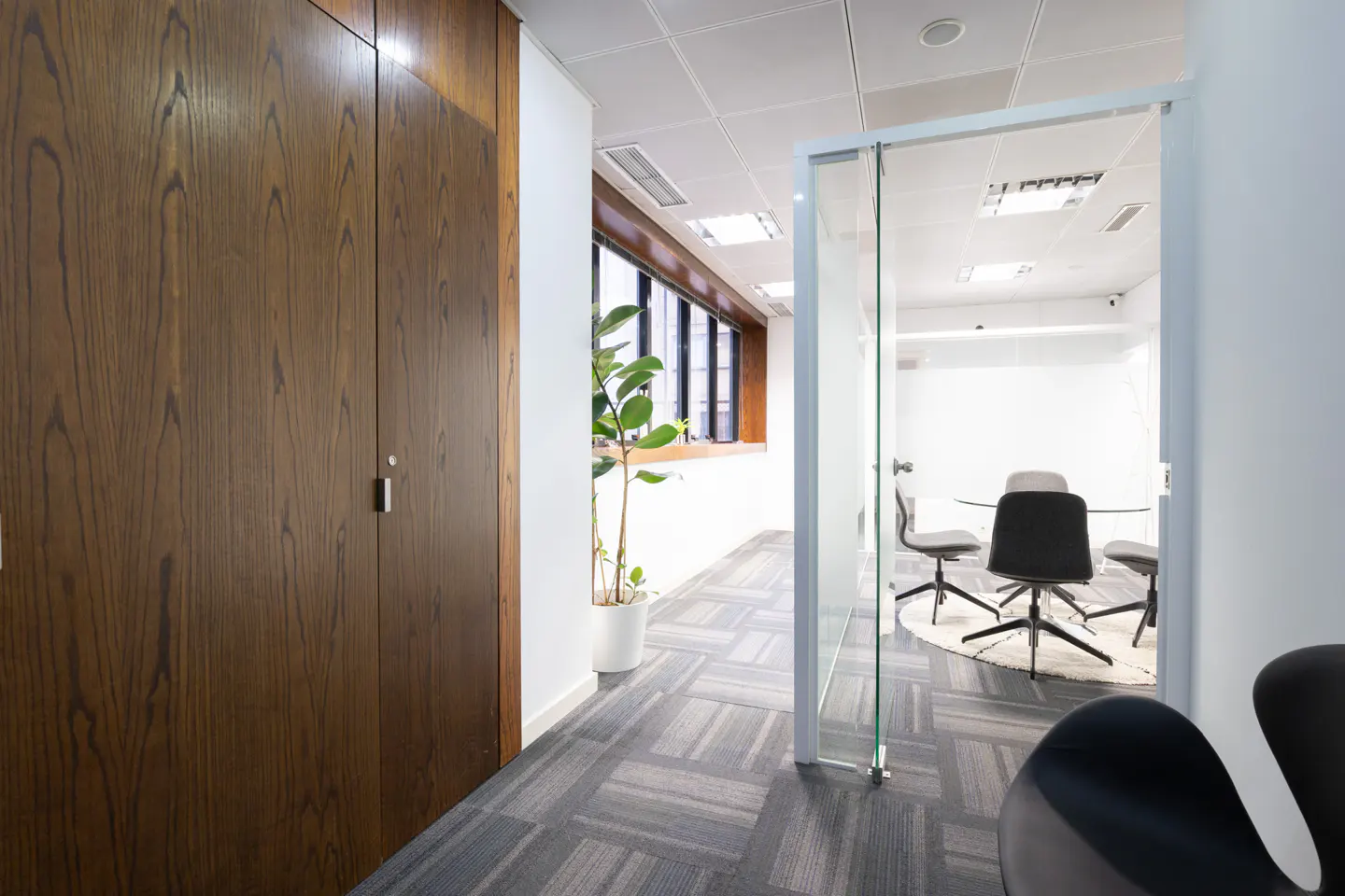 Office interior with wood paneling, gray carpet, and a glass-walled conference room with a round table and chairs.