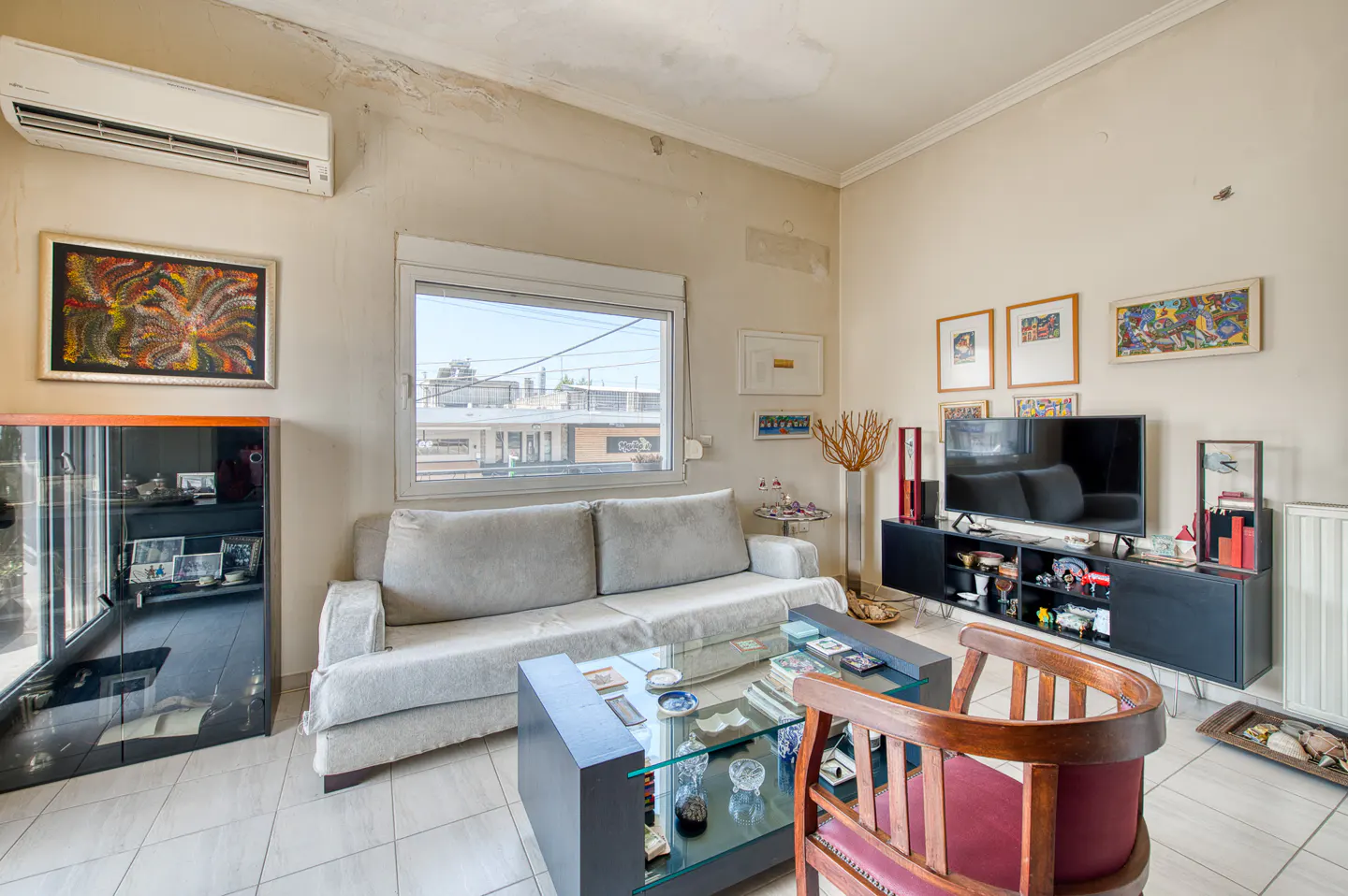Living room with a light gray sofa, glass coffee table, black media console with TV, and a wooden chair with red cushion.