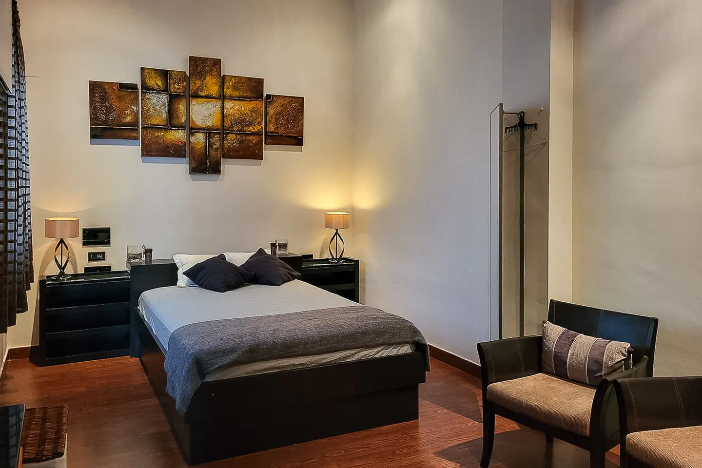 Bedroom with a black platform bed, gray bedding, and abstract art above. Two chairs sit on the wood floor.