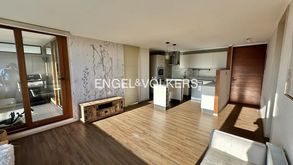 Bright apartment interior with wood floors, white kitchen, and balcony. Engel & Völkers logo on a floral accent wall.