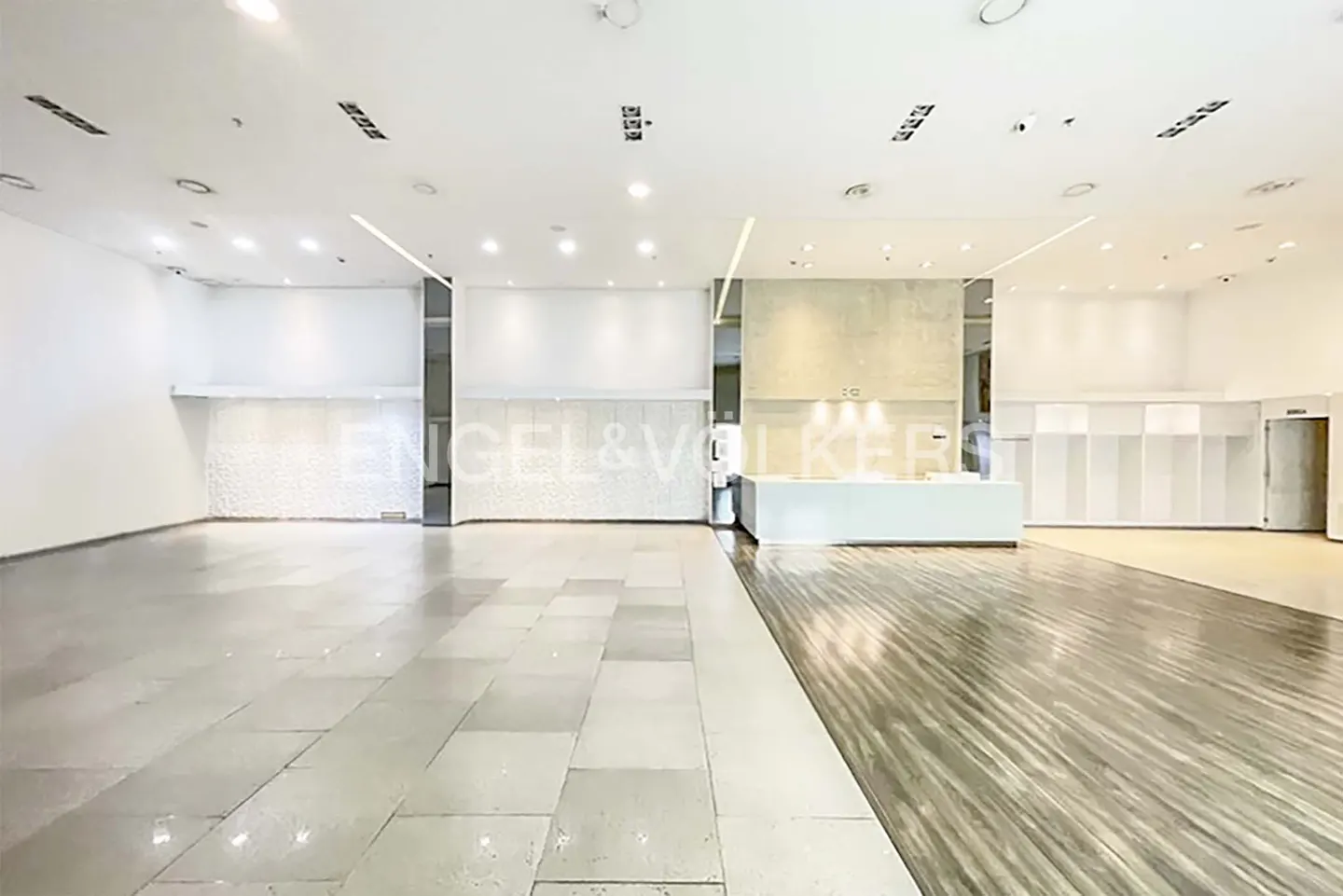 Bright, empty Engel & Volkers office space with white walls, tile and wood floors, and a white reception desk.