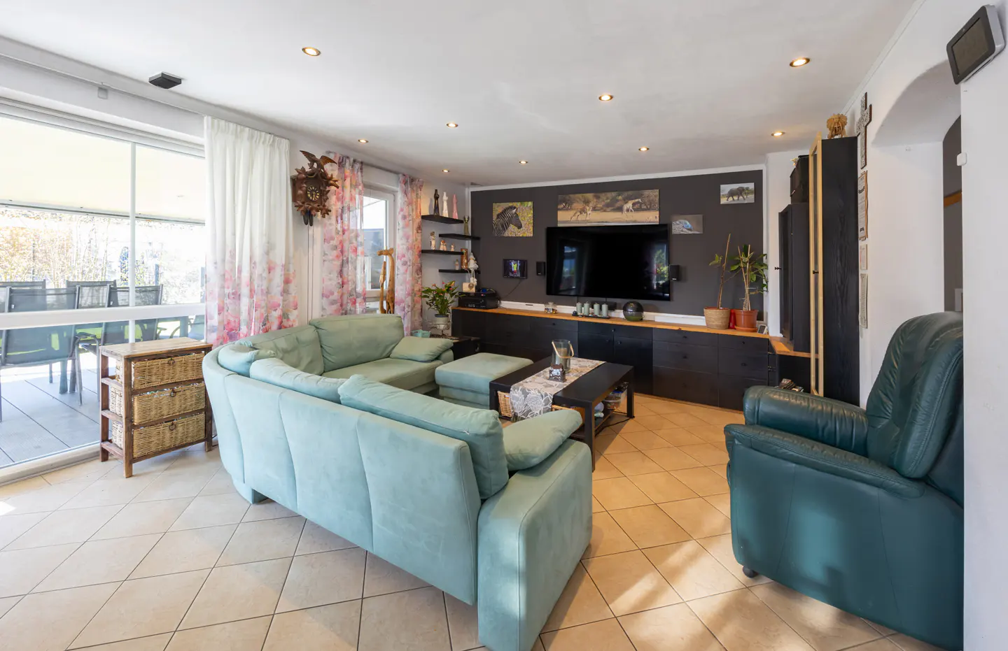 Living room with light blue sectional sofa, dark wood TV console, and a green leather armchair on a tiled floor.