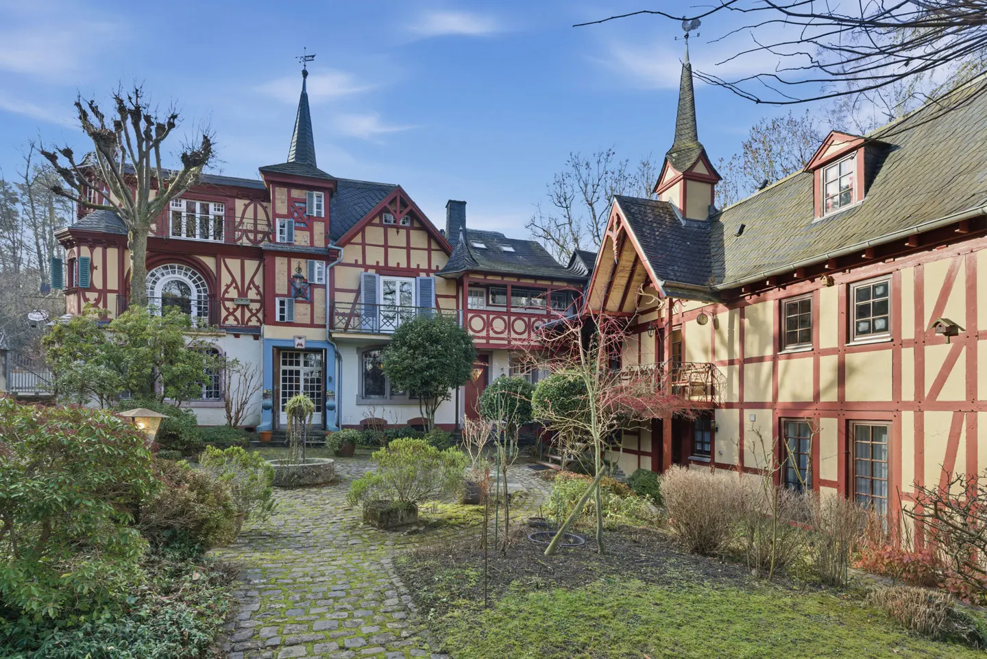 Exterior view of a half-timbered house with a garden, stone path, and trees under a blue sky.