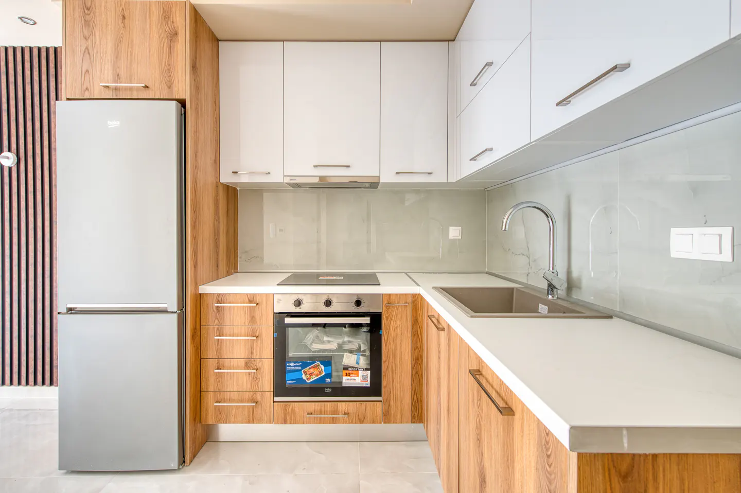 A modern kitchen with white cabinets, wood-grain lower cabinets, stainless steel appliances, and a white countertop.