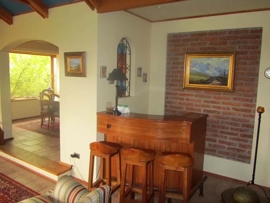 Interior view of a home bar with three wooden stools, a brick accent wall, and a painting of mountains.