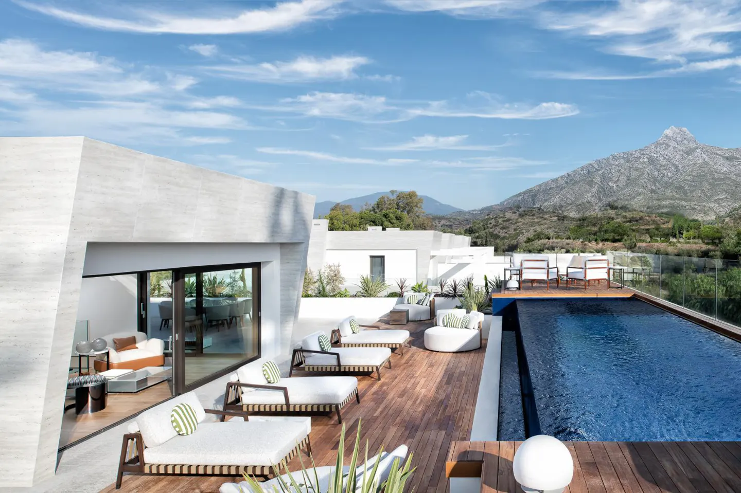 Rooftop patio with lounge chairs, a pool, and mountain views. The patio has a wooden deck and white furniture with green striped pillows.