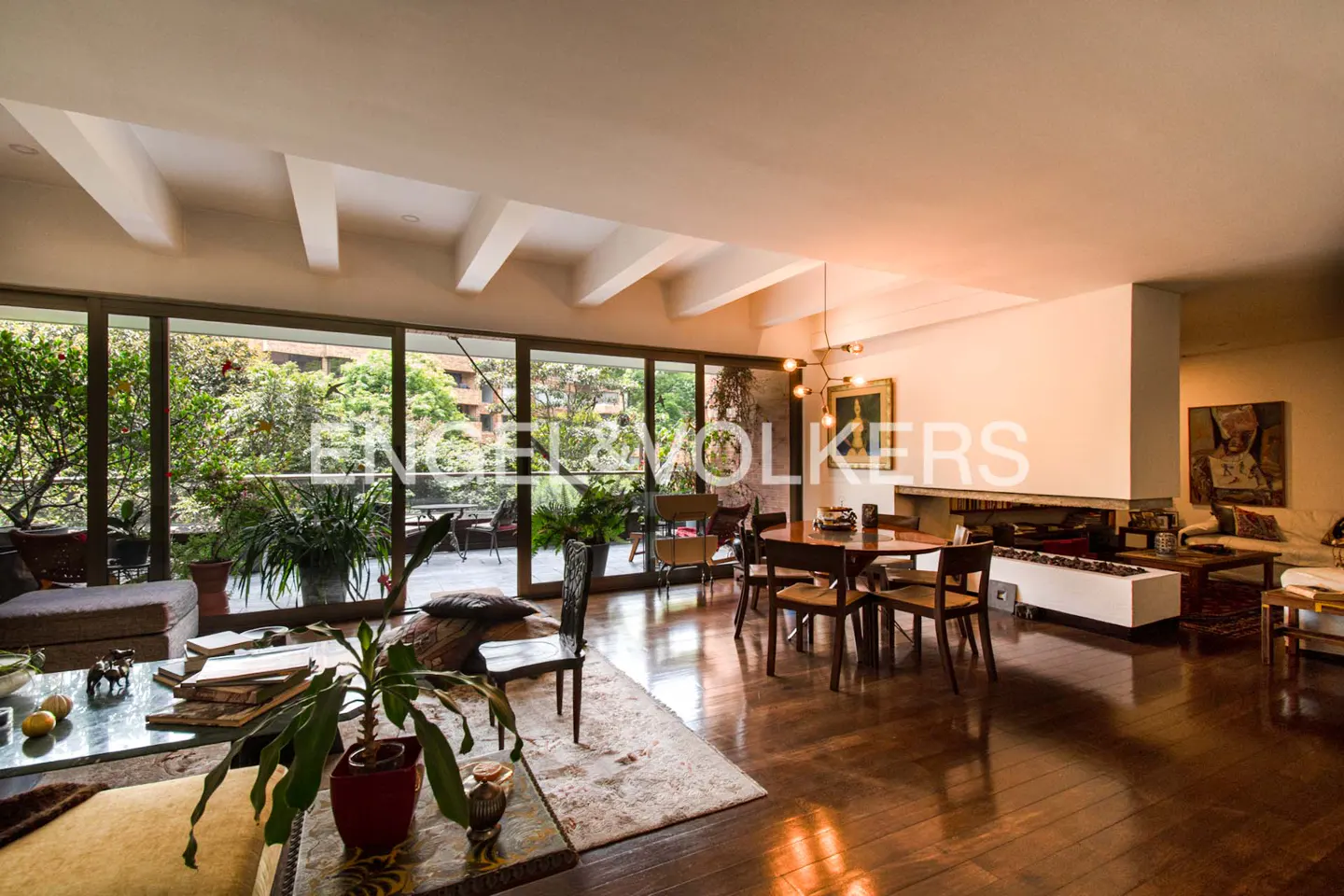 Open-plan living room with hardwood floors, a dining table, and a balcony with lush greenery.