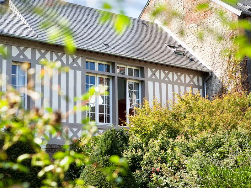 Exterior view of a half-timbered house with white and gray walls, a gray roof, and lush green bushes in front.