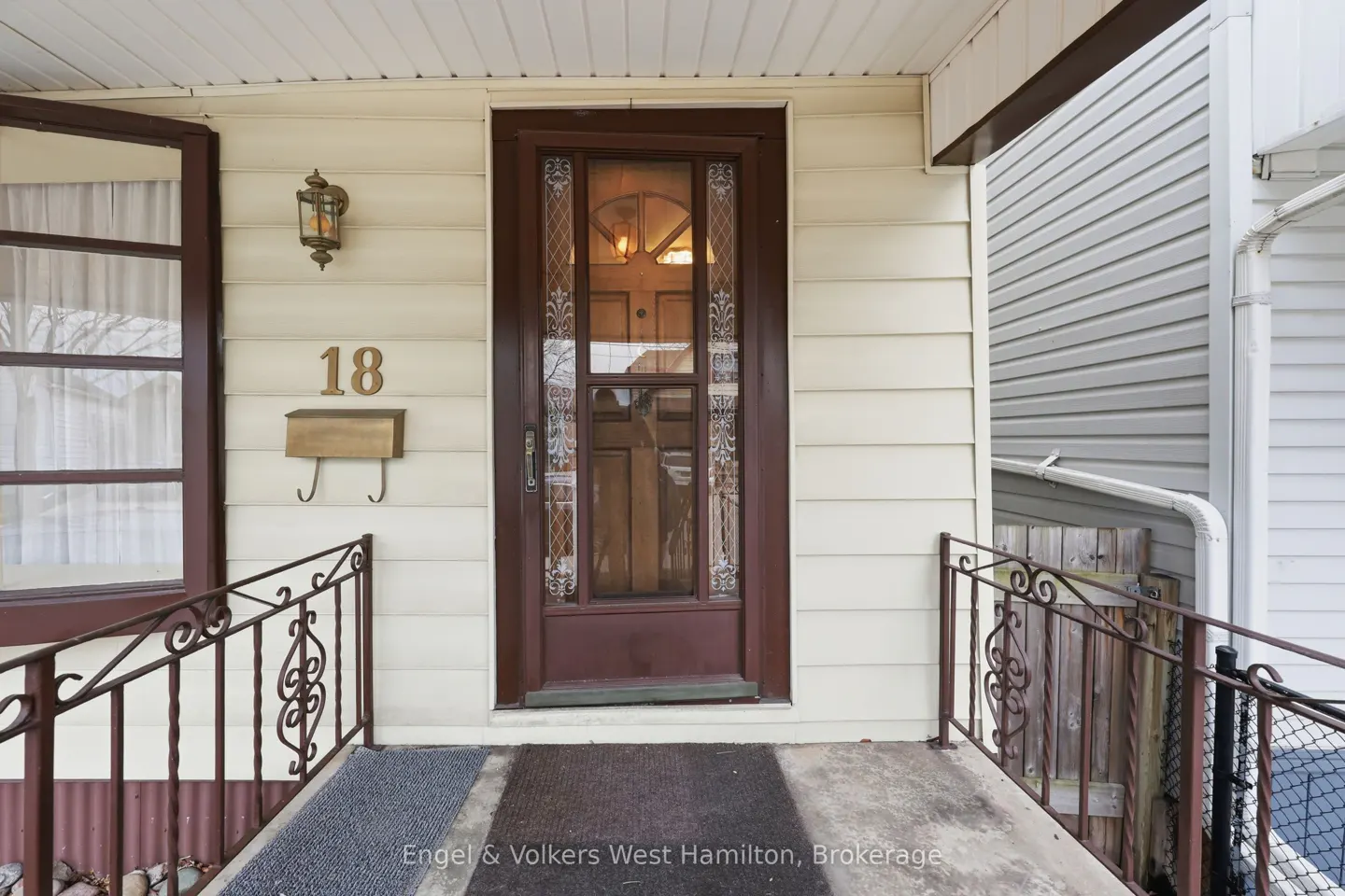 Exterior view of a house entrance with a brown door, house number 18, a mailbox, and a wrought iron railing.