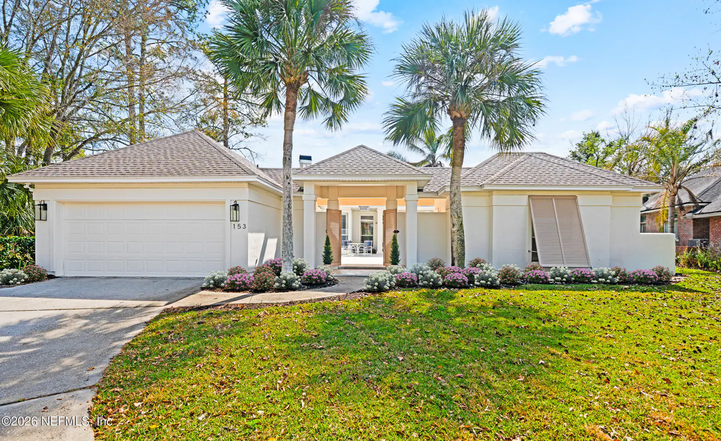 A one-story white house with a gray roof, palm trees, and a green lawn.