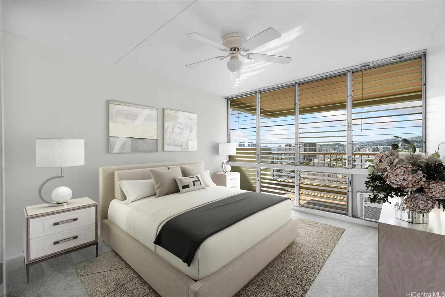 Modern bedroom with a queen bed, white walls, ceiling fan, and large windows overlooking a city view with wood blinds.