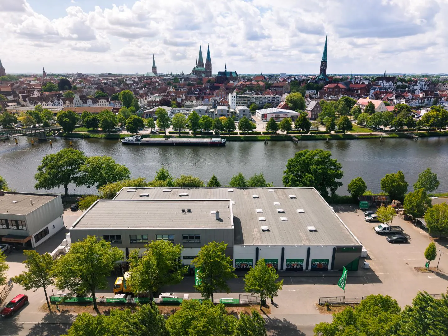 Aerial view of a gray commercial building near a river, with a city skyline featuring church spires in the background.