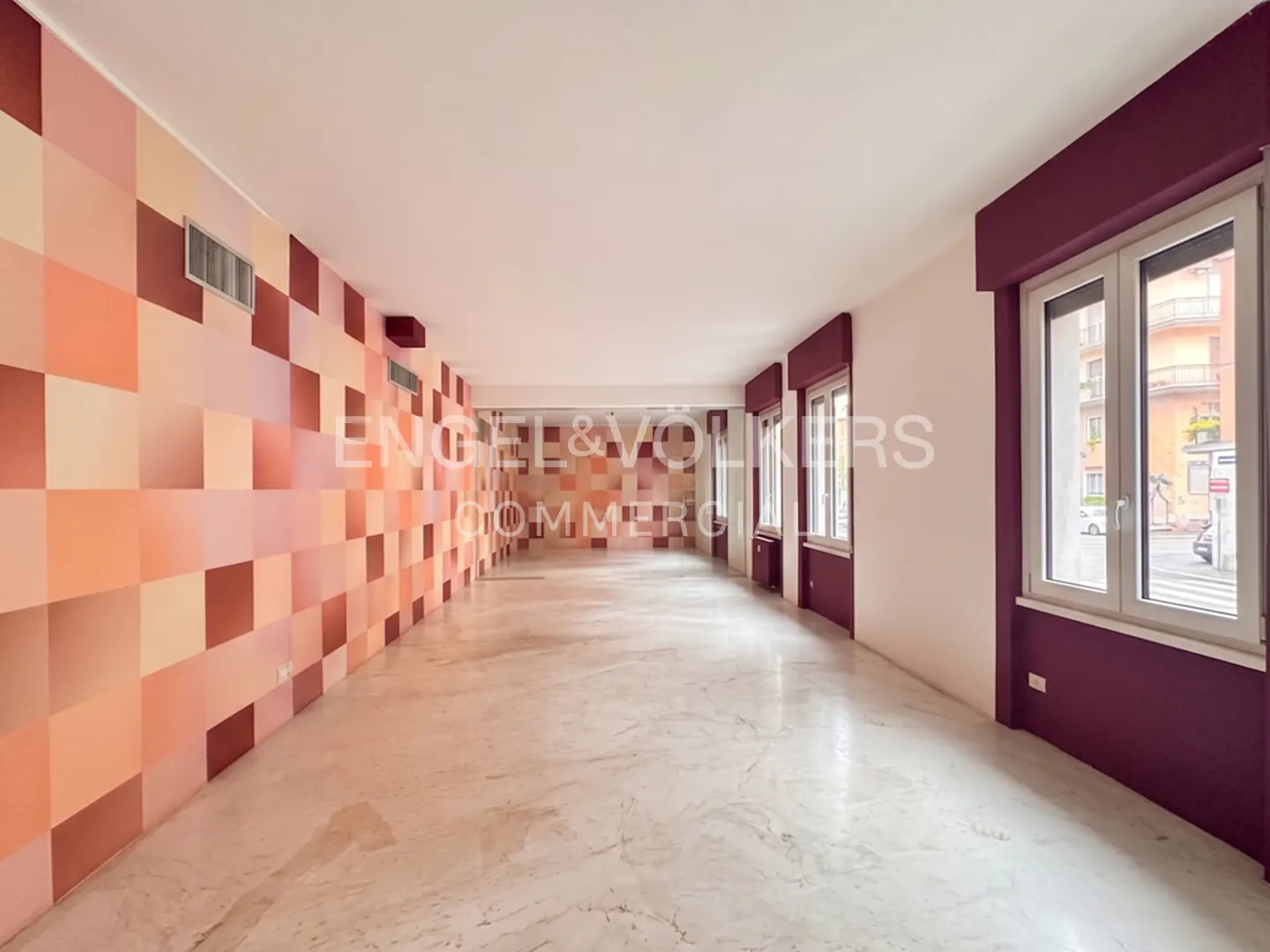 Empty room with marble floors, a wall with peach and brown squares, and windows with maroon trim.