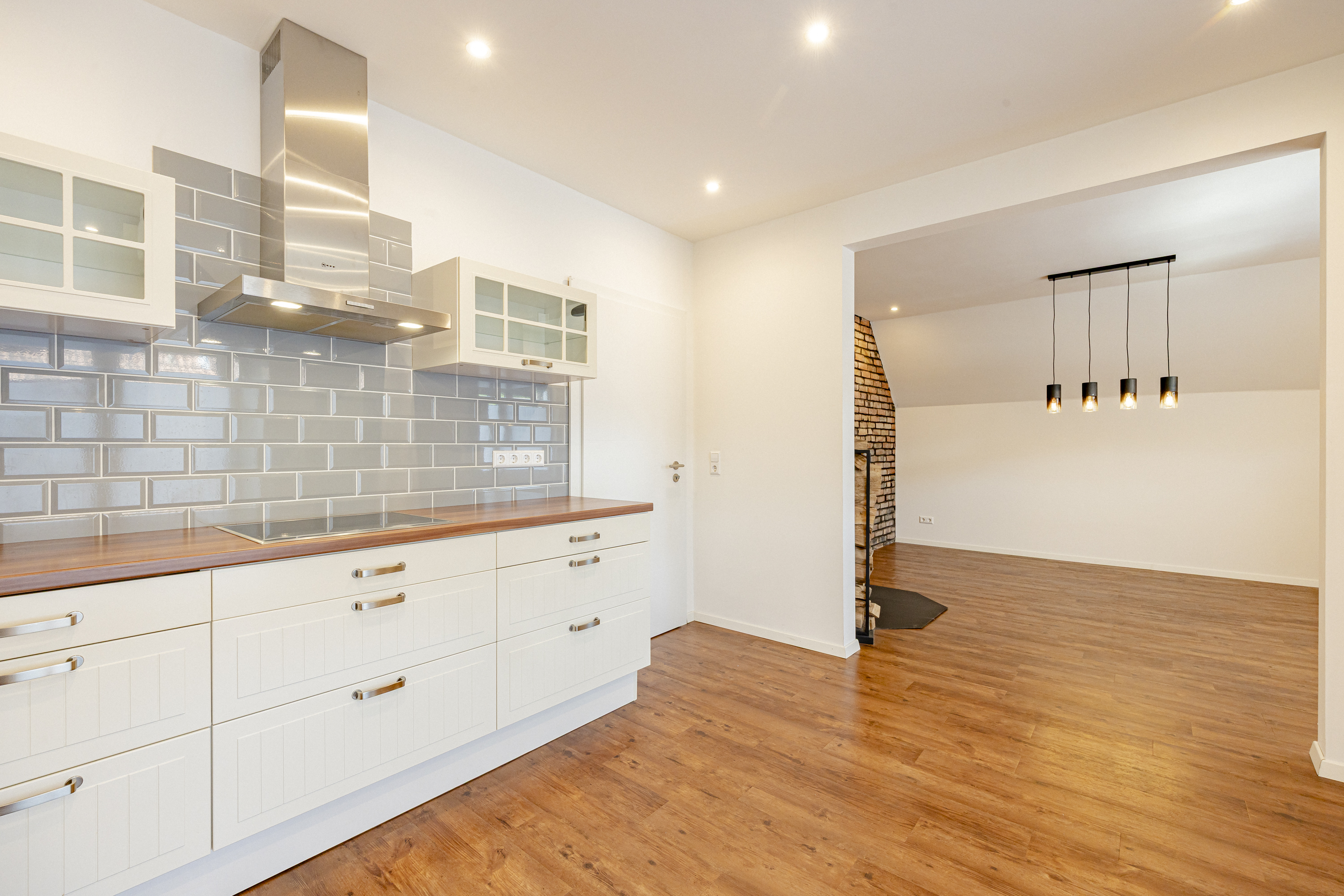 Modern kitchen with white cabinets, wood countertops, and gray subway tile backsplash, opening into a dining area. [AI-generated text]