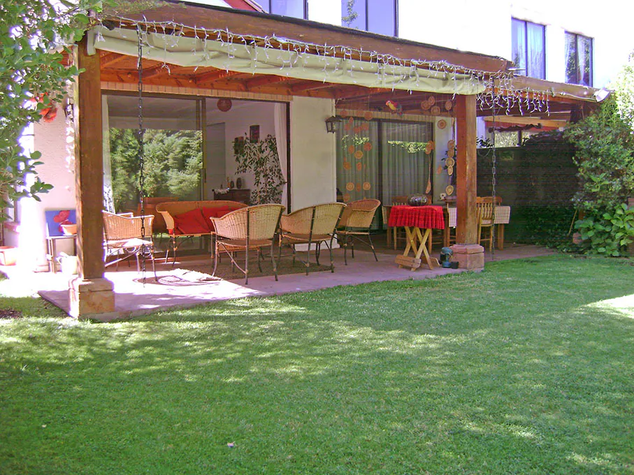 Outdoor patio with wicker furniture, a red tablecloth, and string lights, leading to a green lawn.