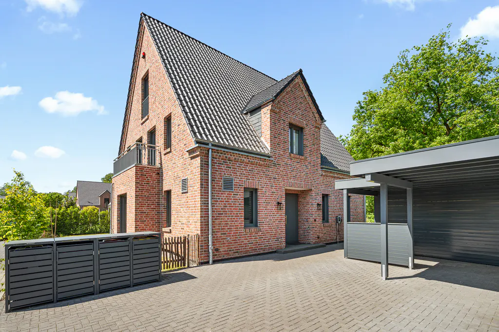 A two-story brick house with a dark gray roof, gray window frames, and a gray carport on a paved driveway.
