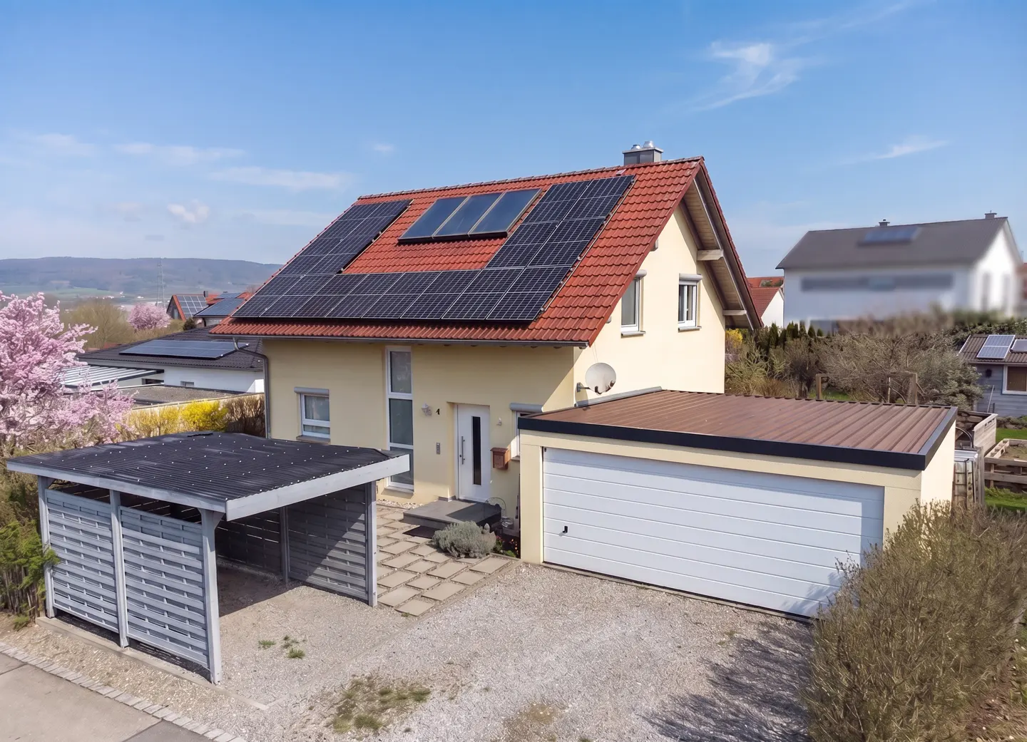 A tan house with a red roof and solar panels, a garage, and a carport on a sunny day.