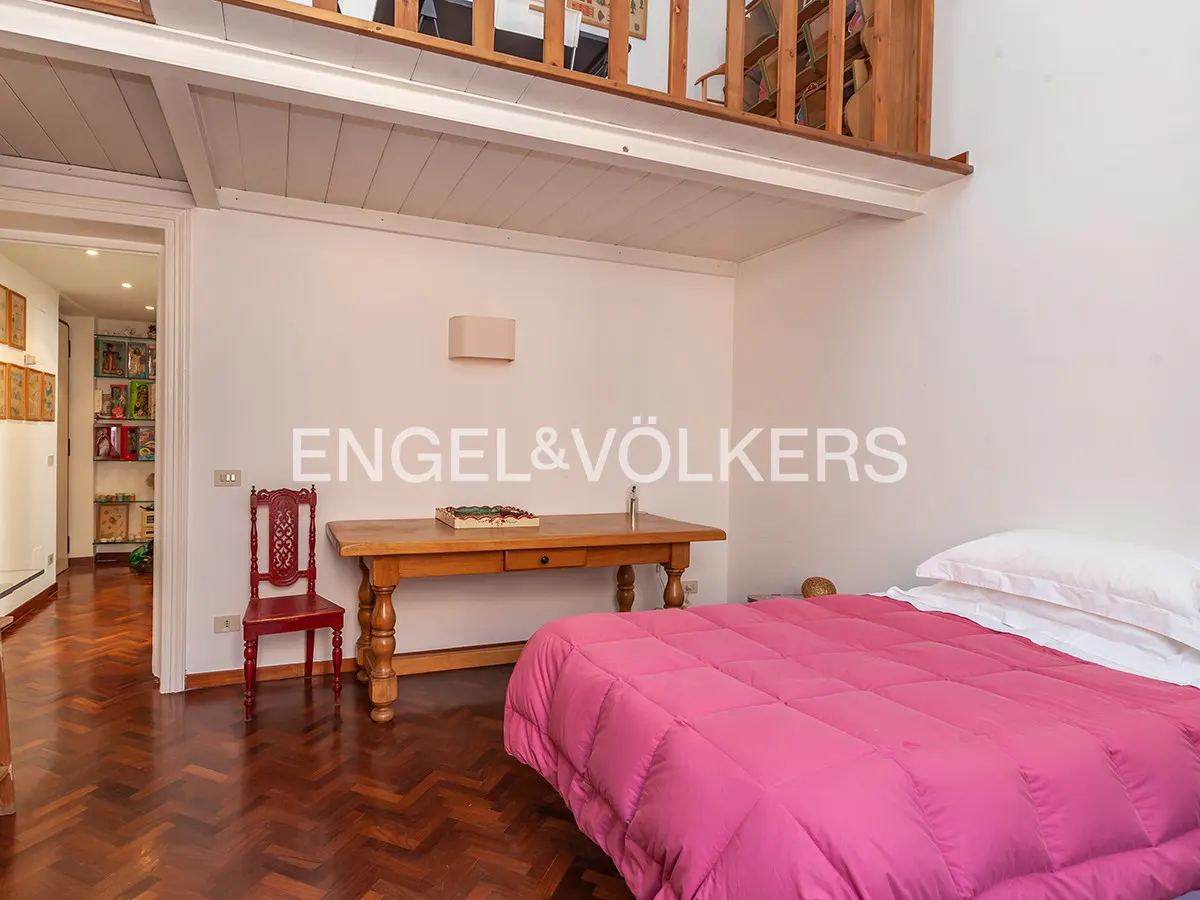 Bedroom with pink comforter, white walls, and wood floors. A desk and red chair sit near the bed. A loft is above.