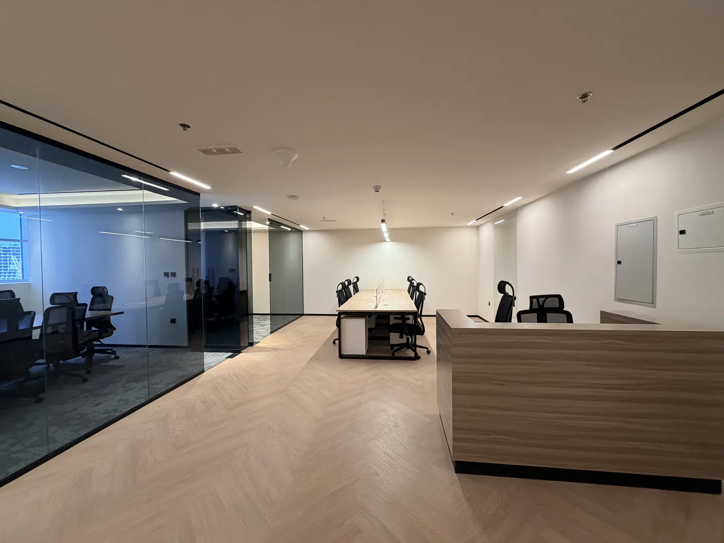 A modern office space with a reception desk, conference room with glass walls, and herringbone wood floors.