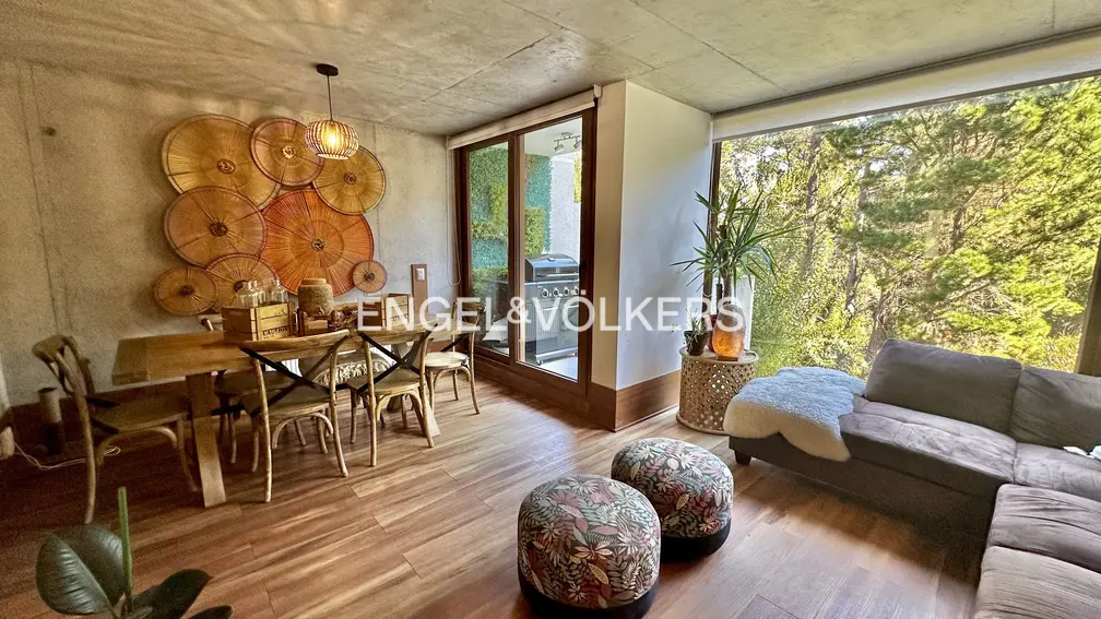 A modern living and dining area with wood floors, a dining table, and a gray sofa with a view of trees.