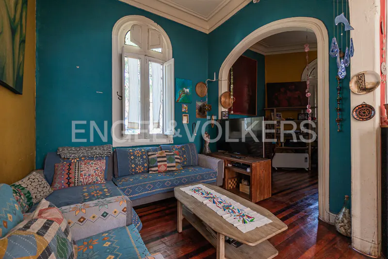 A living room with blue walls, a blue sofa with patterned pillows, and a wooden coffee table. An arched doorway leads to another room.