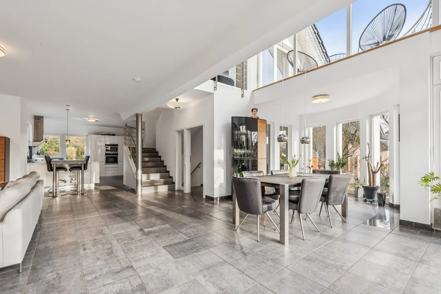 Bright, open-plan living space with gray tile flooring, white walls, a dining table with gray chairs, and a modern kitchen.