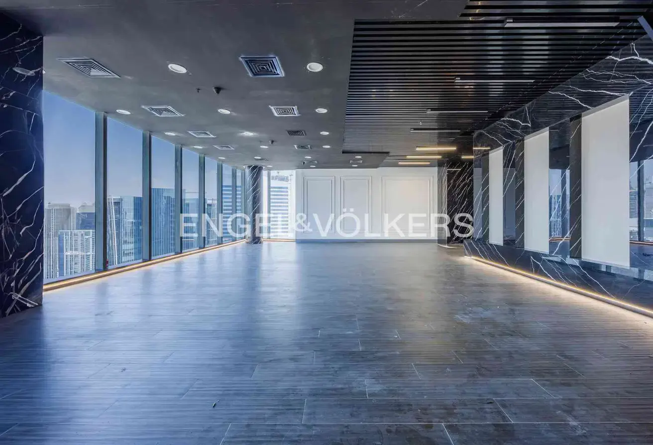 An empty office space with marble columns, a dark gray floor, and floor-to-ceiling windows with a city view.