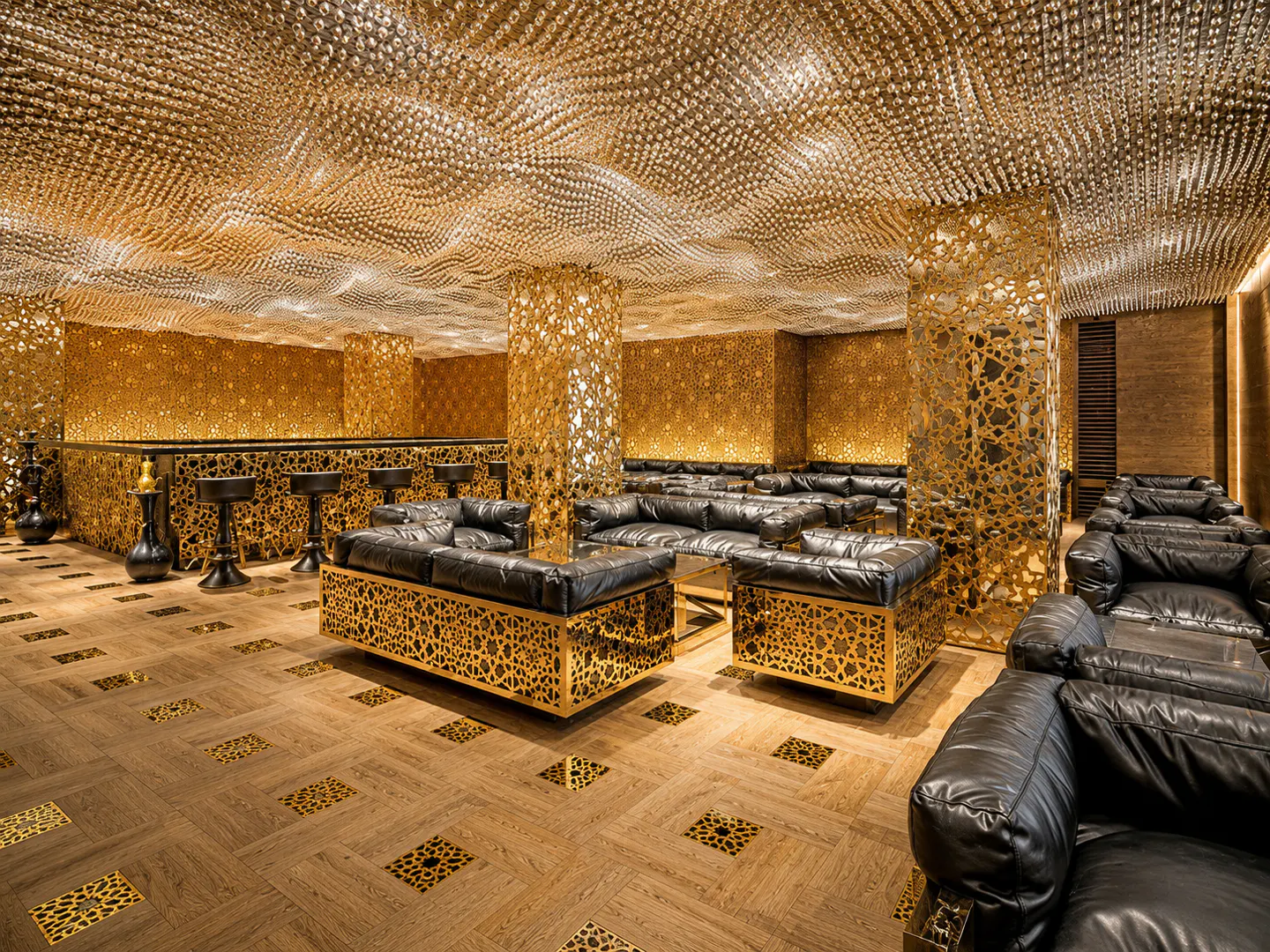 Opulent lounge with black leather sofas, gold lattice details, and a shimmering, textured gold ceiling. Bar area visible in the background.