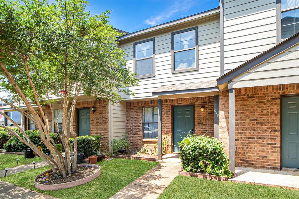 Exterior of a two-story townhouse with brick and siding, green door, and a tree in the front yard.