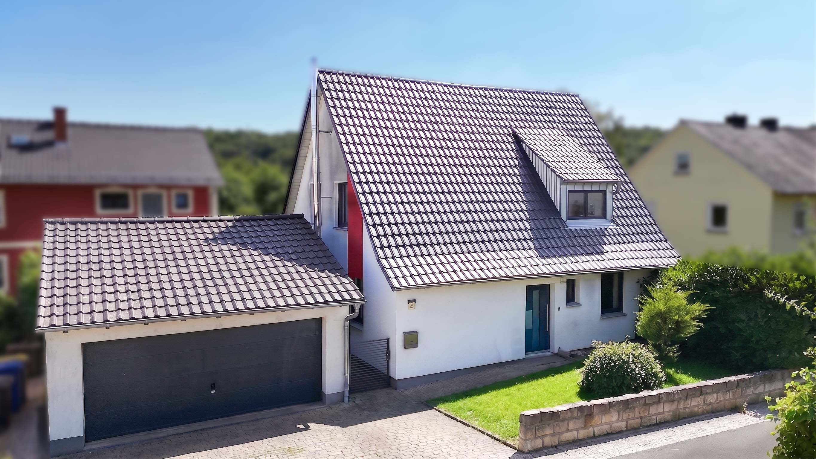 White two-story house with a dark tiled roof, attached garage, and a small front lawn under a clear blue sky.
