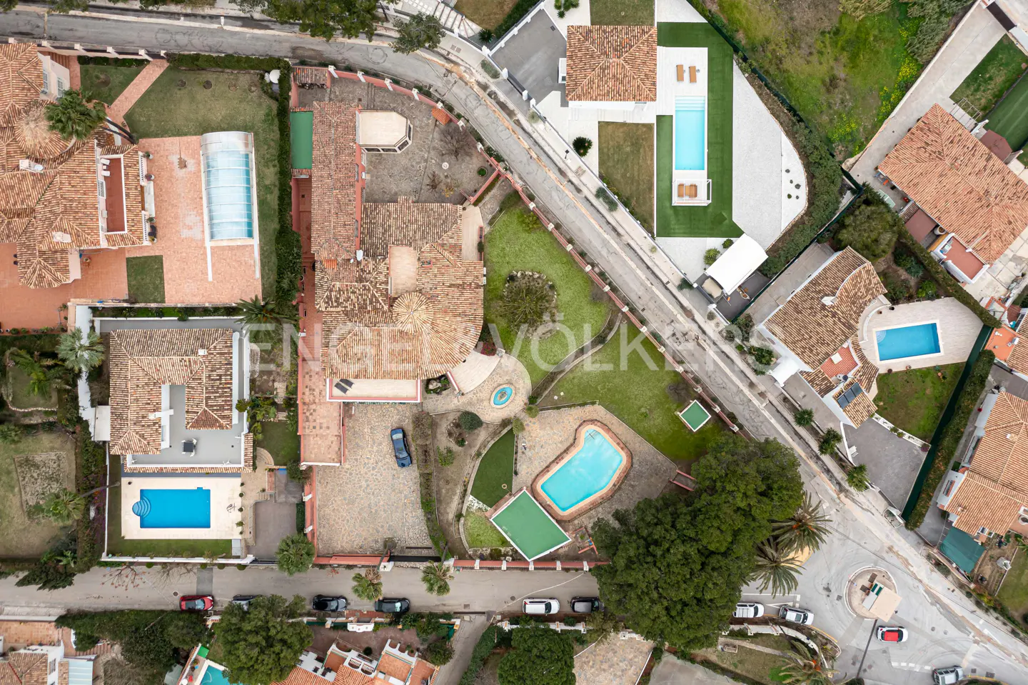 Aerial view of luxury homes with terracotta roofs, green lawns, and blue pools in a residential neighborhood.