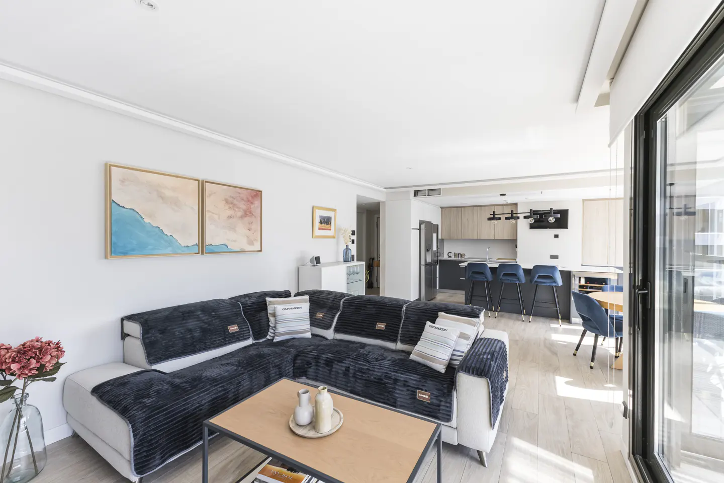 Bright living room with a large sectional sofa, wood coffee table, and open kitchen in the background.