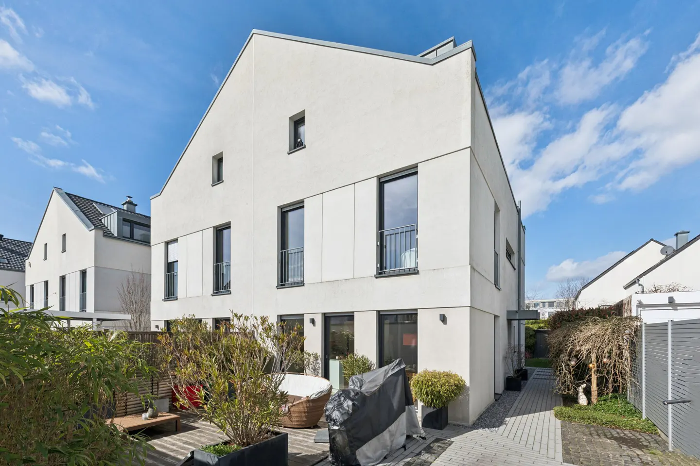 Exterior view of a modern, white townhouse with black framed windows and a small backyard patio with plants.