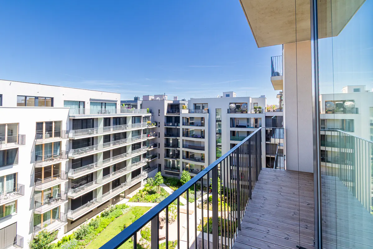 View from a wooden balcony overlooking a modern apartment complex with white buildings and a central green courtyard.