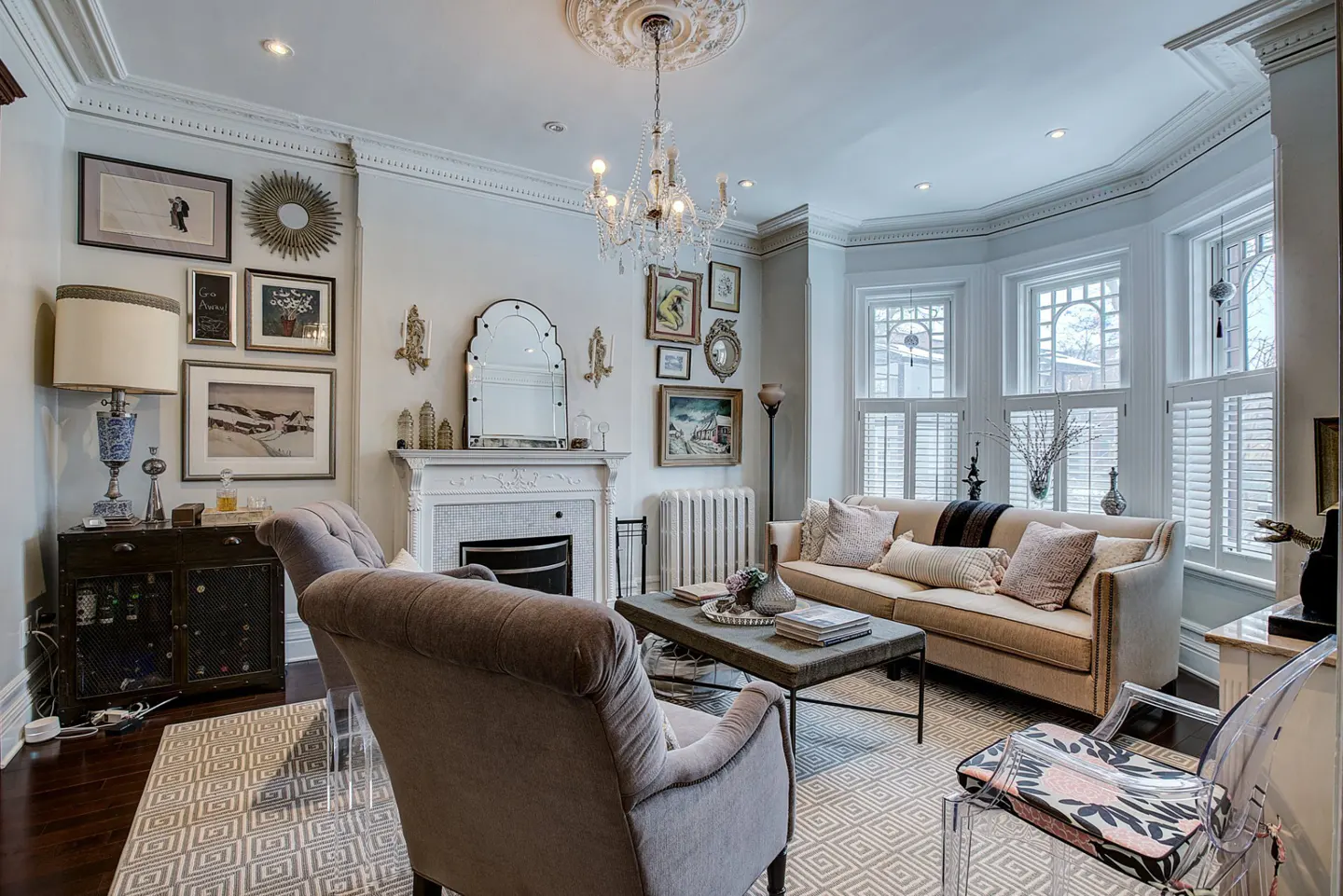 A living room with a beige sofa, two gray armchairs, and a fireplace. A chandelier hangs from the ceiling.