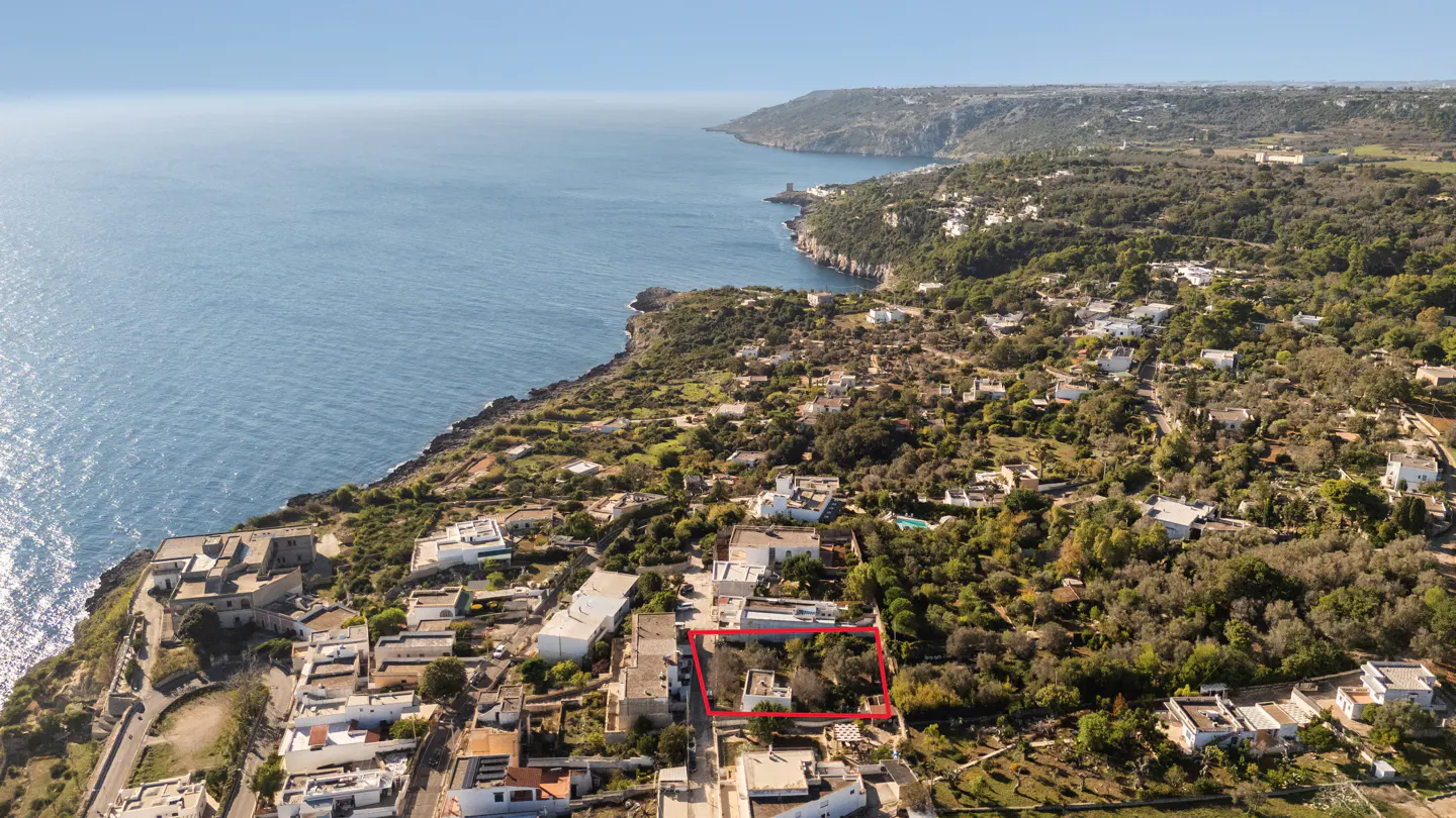 Aerial view of a property outlined in red, near the coast with blue ocean and green vegetation.
