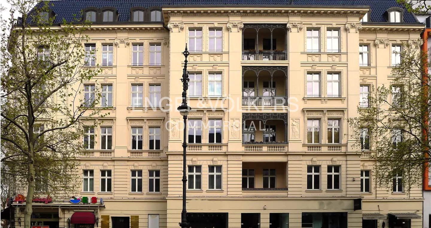 A tan, ornate building with many windows and wrought iron balconies. Trees frame the sides of the building.