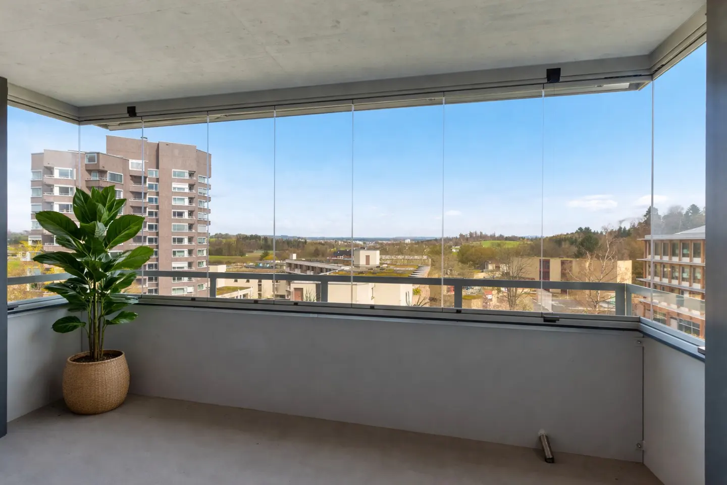 A balcony with glass walls, a potted plant, and a city view.