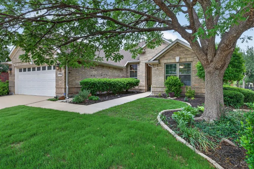 Tan brick house with a white garage door, green lawn, and a large tree in the front yard.