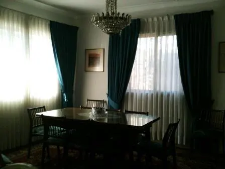 A dining room with a dark wood table and chairs, a crystal chandelier, and teal curtains.