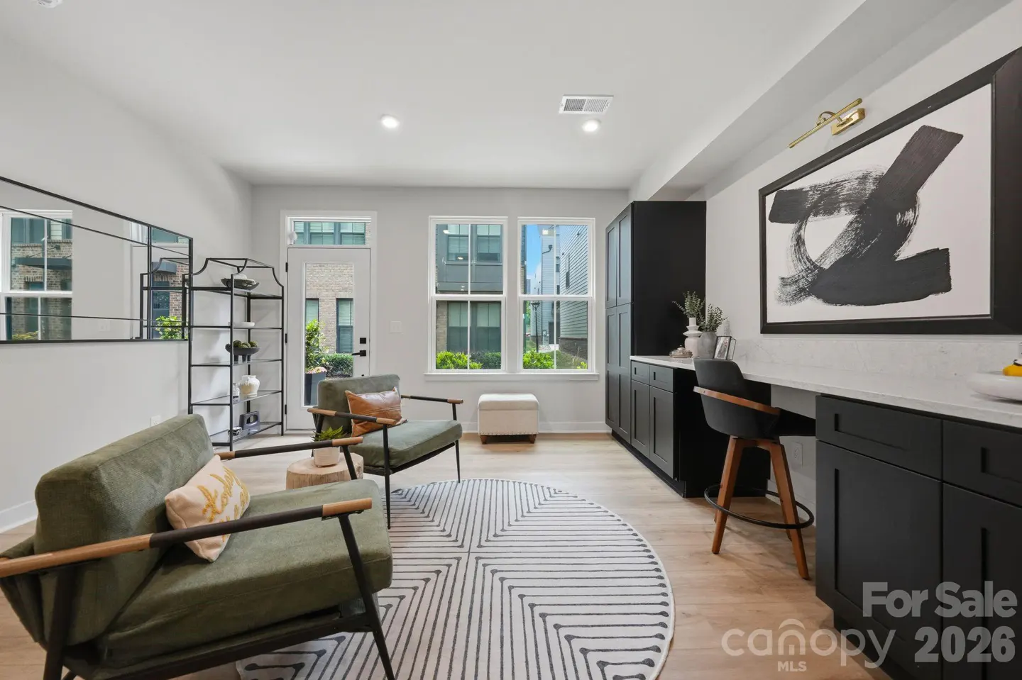 Bright living room with green chairs, a black and white rug, and a black built-in desk area with a modern art piece.
