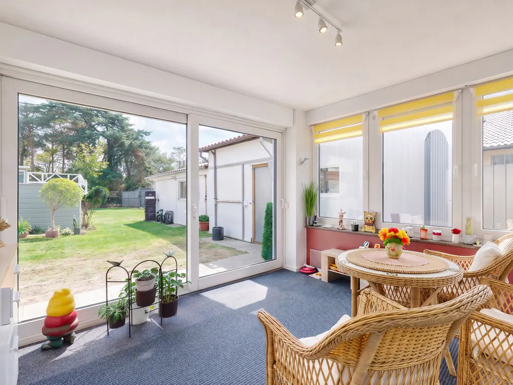 Bright sunroom with wicker chairs and table, blue carpet, and sliding glass doors to a green backyard. Yellow blinds on windows.