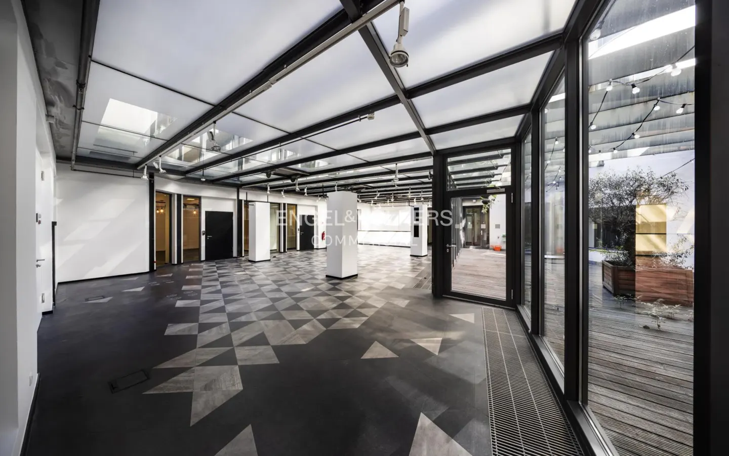 Bright, modern office space with black and gray geometric floor, glass ceiling, and large windows to an outdoor patio.