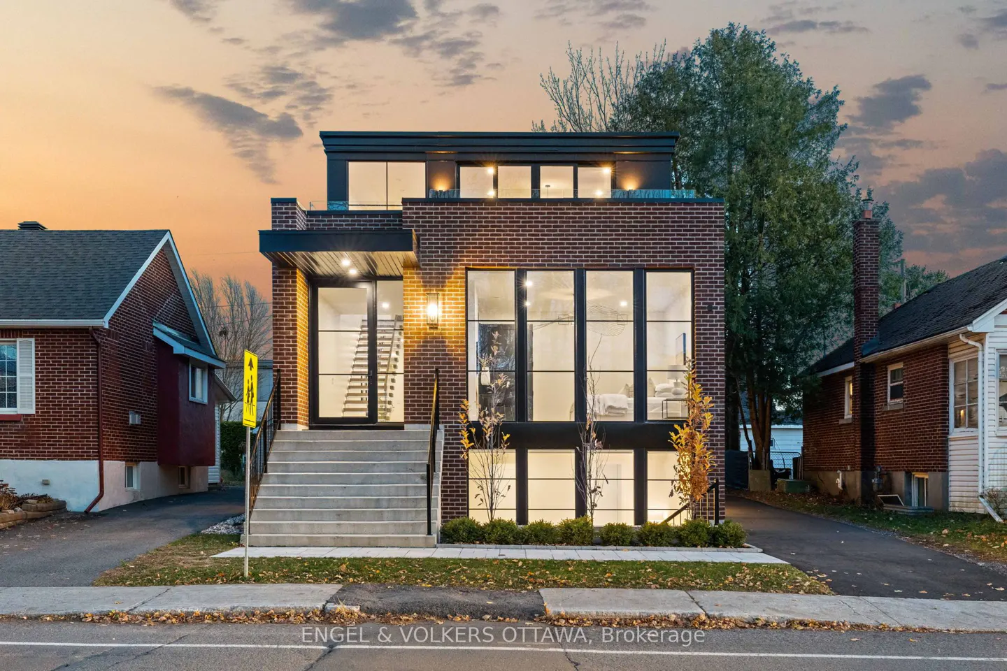 Modern brick house with large windows and a black trim, featuring a staircase leading to the front door.