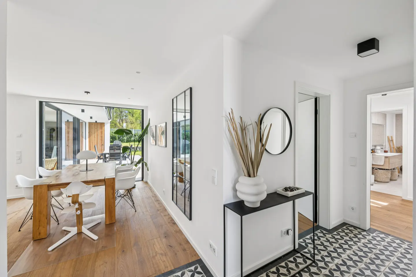 Bright, modern home interior with white walls, wood floors, and black/white patterned tile. A dining table and console table are visible.