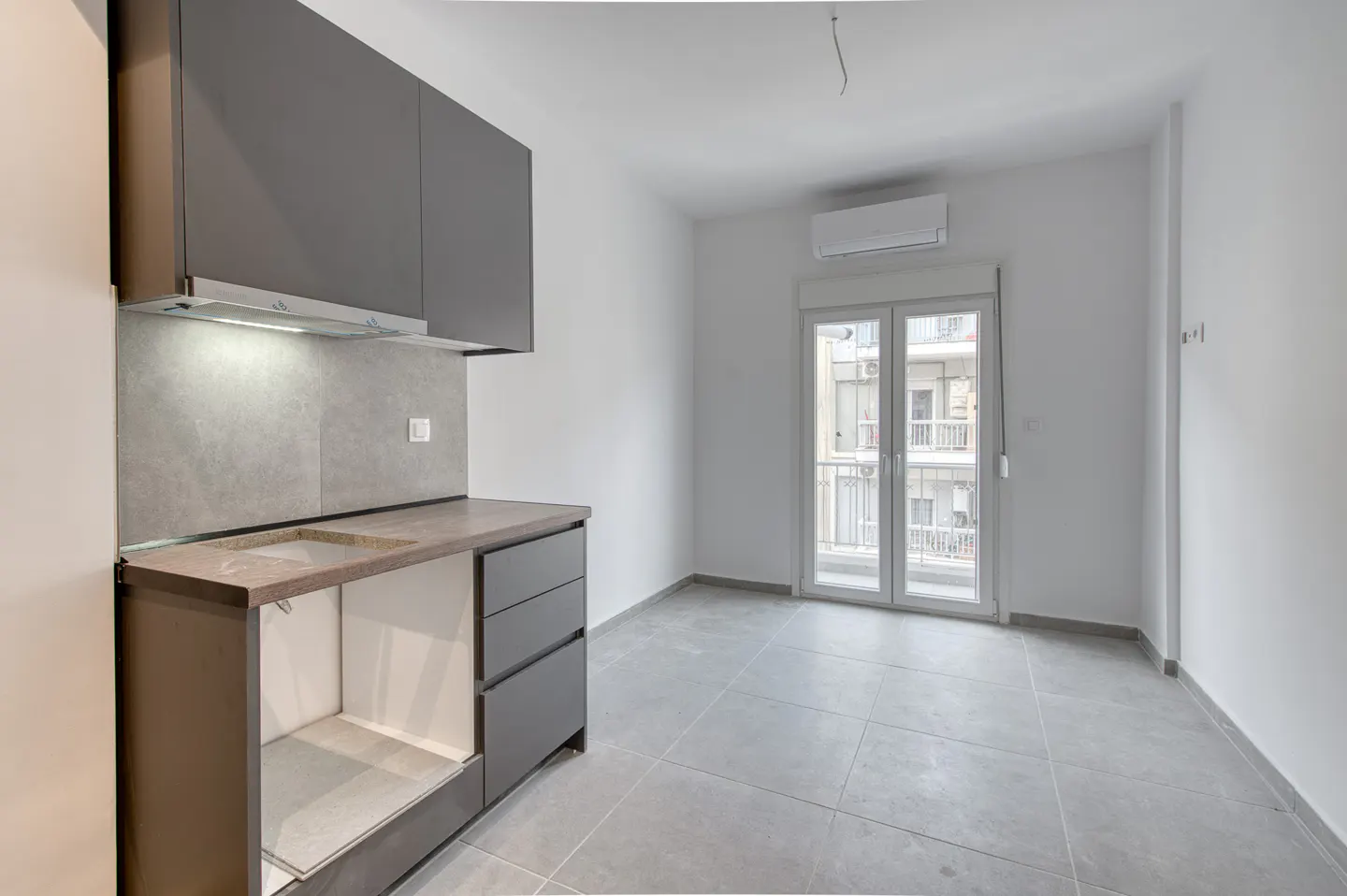 A modern, empty apartment with gray cabinets, a sink, and a balcony with a view of a building.