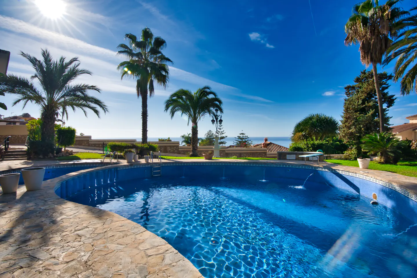 A blue swimming pool with palm trees and a blue sky in the background.