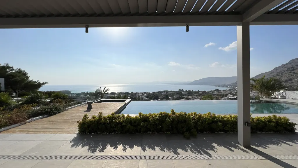 View from a modern patio overlooking an infinity pool and the ocean on a sunny day.